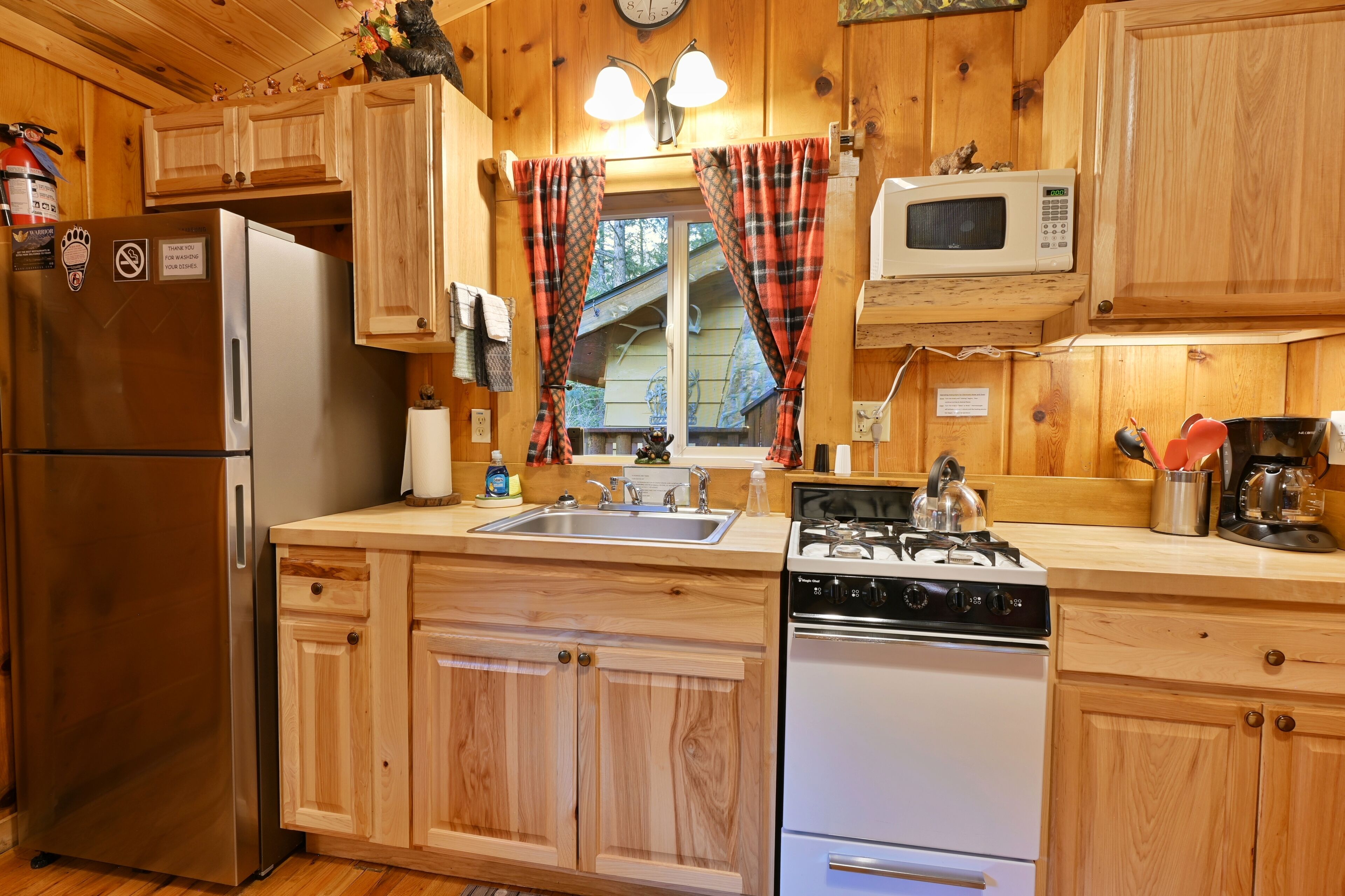 A kitchen with wooden cabinets, a stainless steel refrigerator, a microwave, a stove, and a sink.