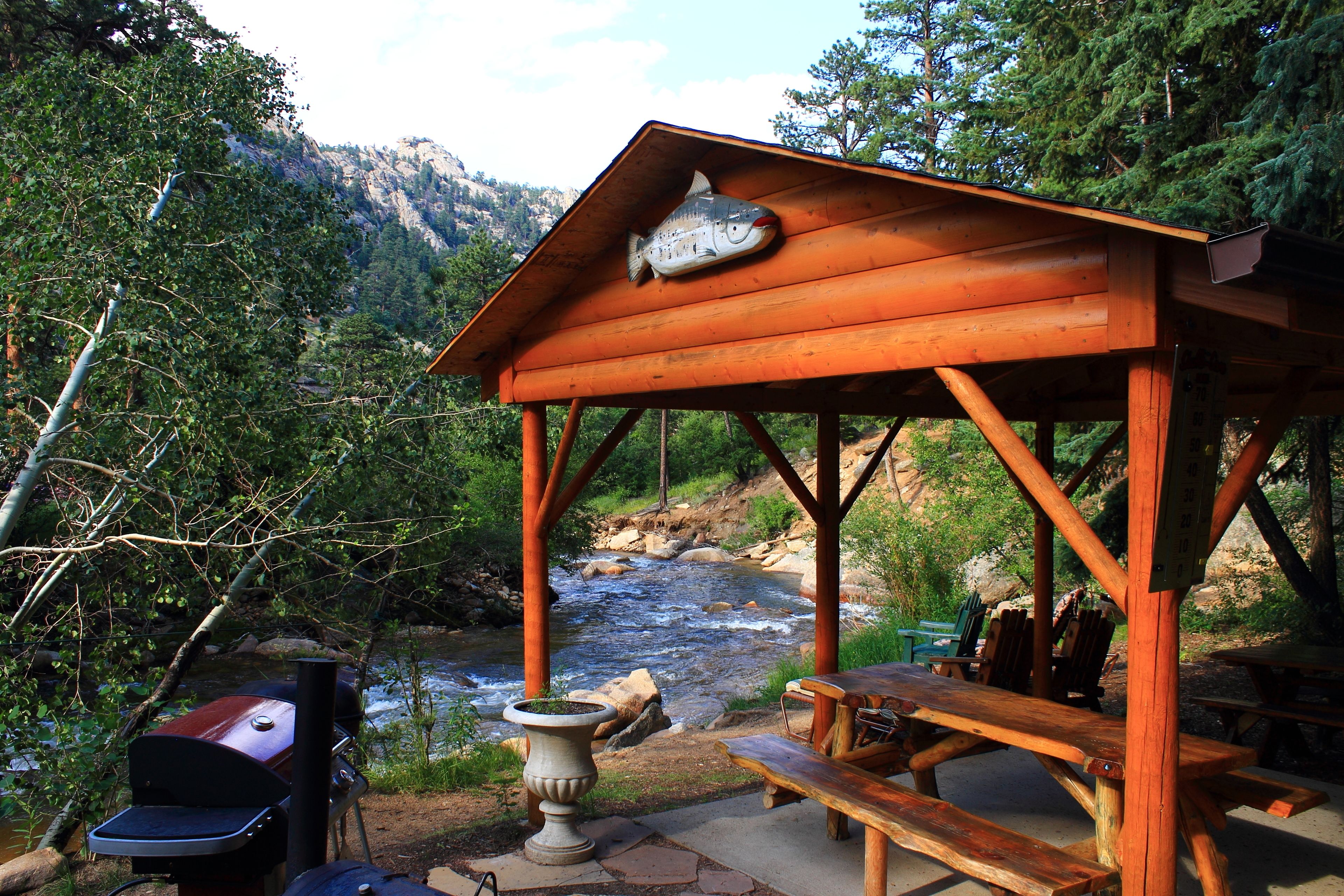 A wooden gazebo with a fish sculpture, overlooking a river and surrounded by trees.