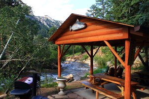 A wooden gazebo with a fish sculpture, overlooking a river and surrounded by trees.