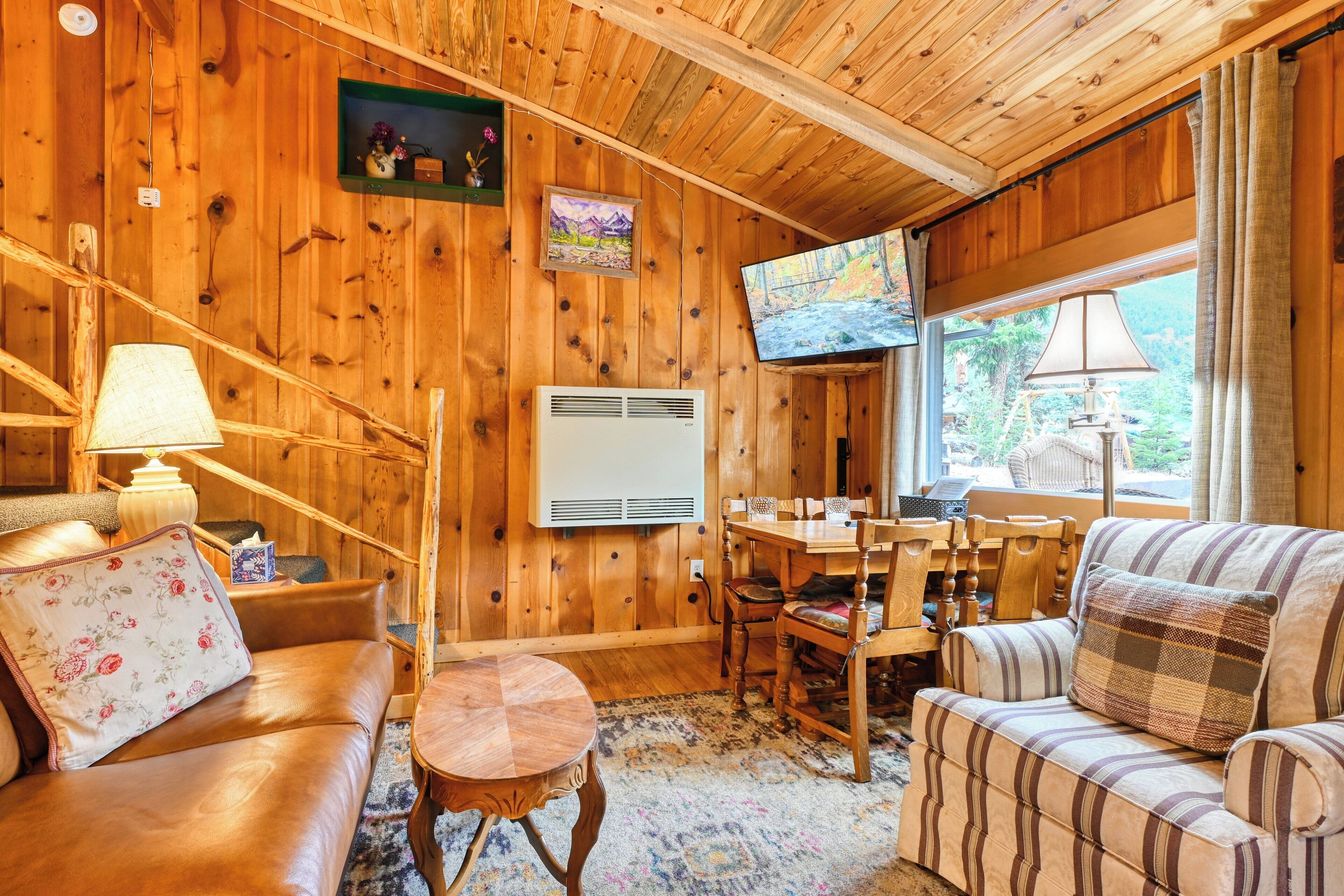 Interior acogedor de una cabaña con detalles de madera, un sofá, una mesa de comedor y un televisor.