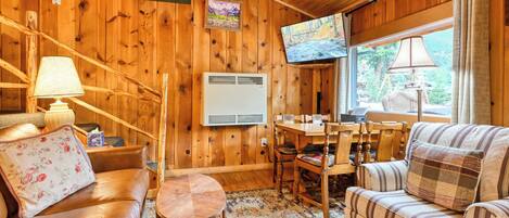 Interior acogedor de una cabaña con detalles de madera, un sofá, una mesa de comedor y un televisor.