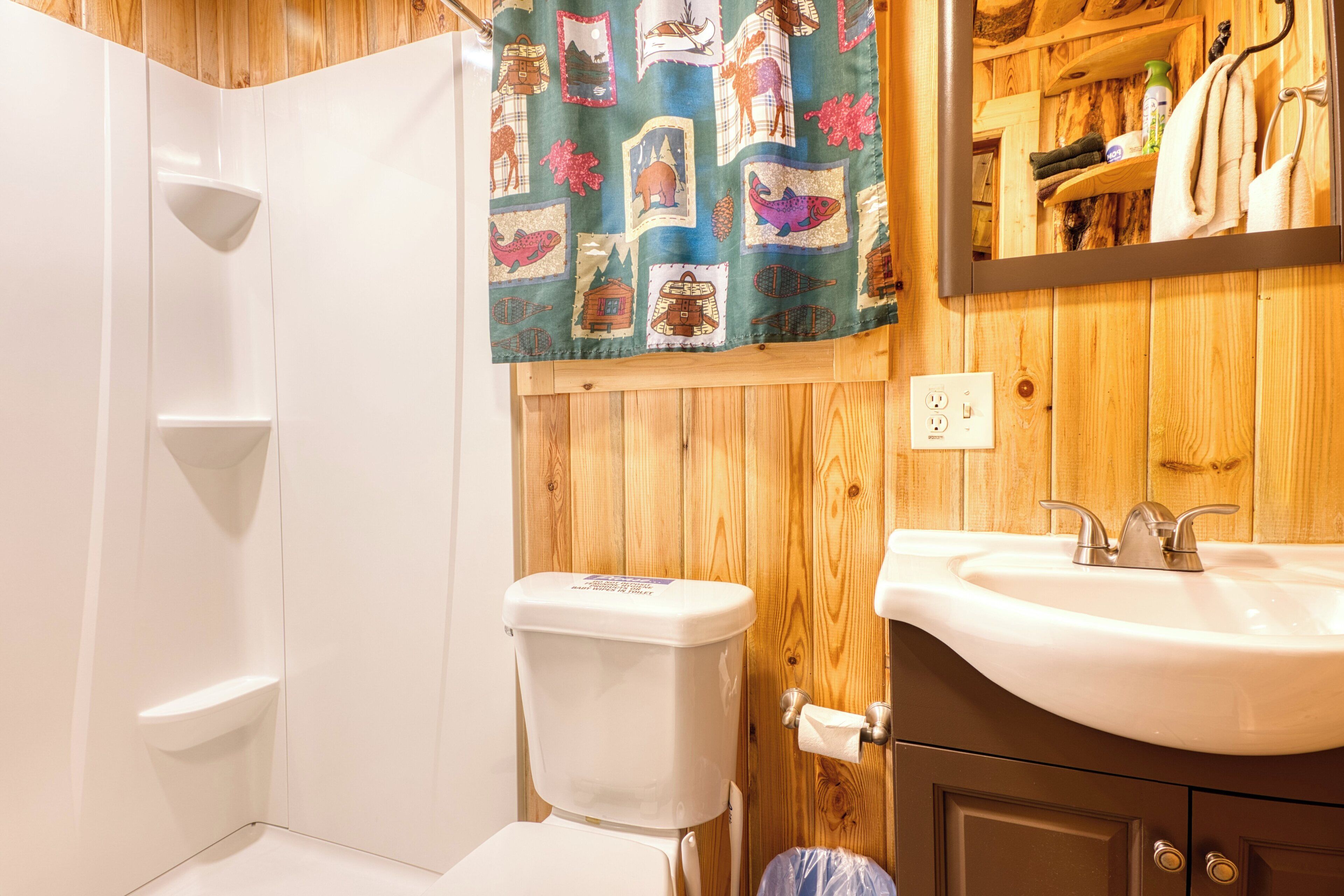 A bathroom with a wooden wall, a white toilet, a sink, and a shower.