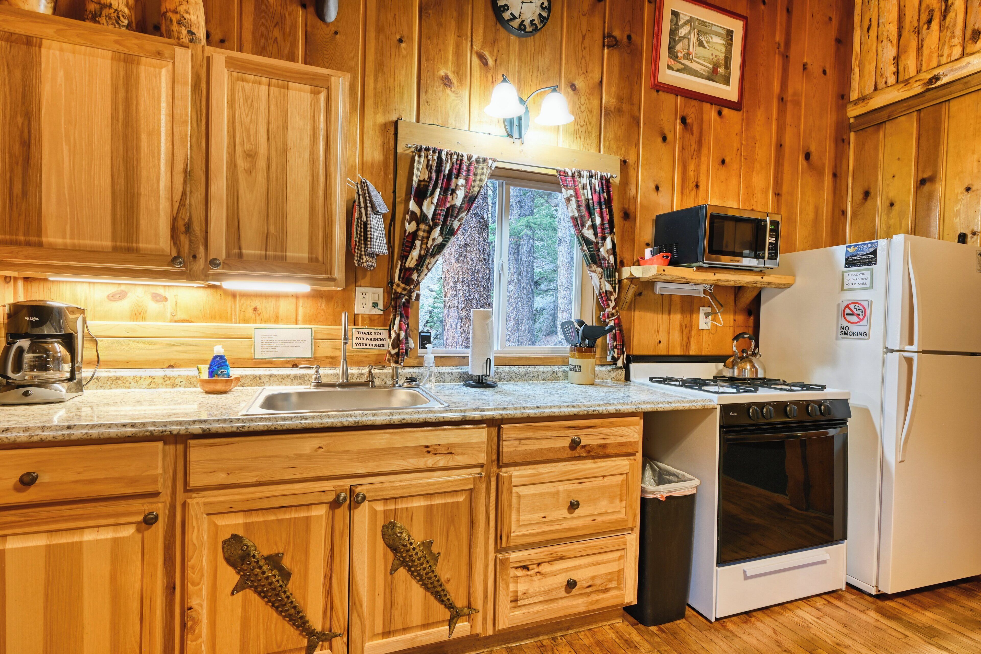 Une cuisine rustique aménagée dans une cabane en bois, avec un poêle, un four à micro-ondes et un réfrigérateur. On y trouve des placards en bois et une fenêtre avec des rideaux.
