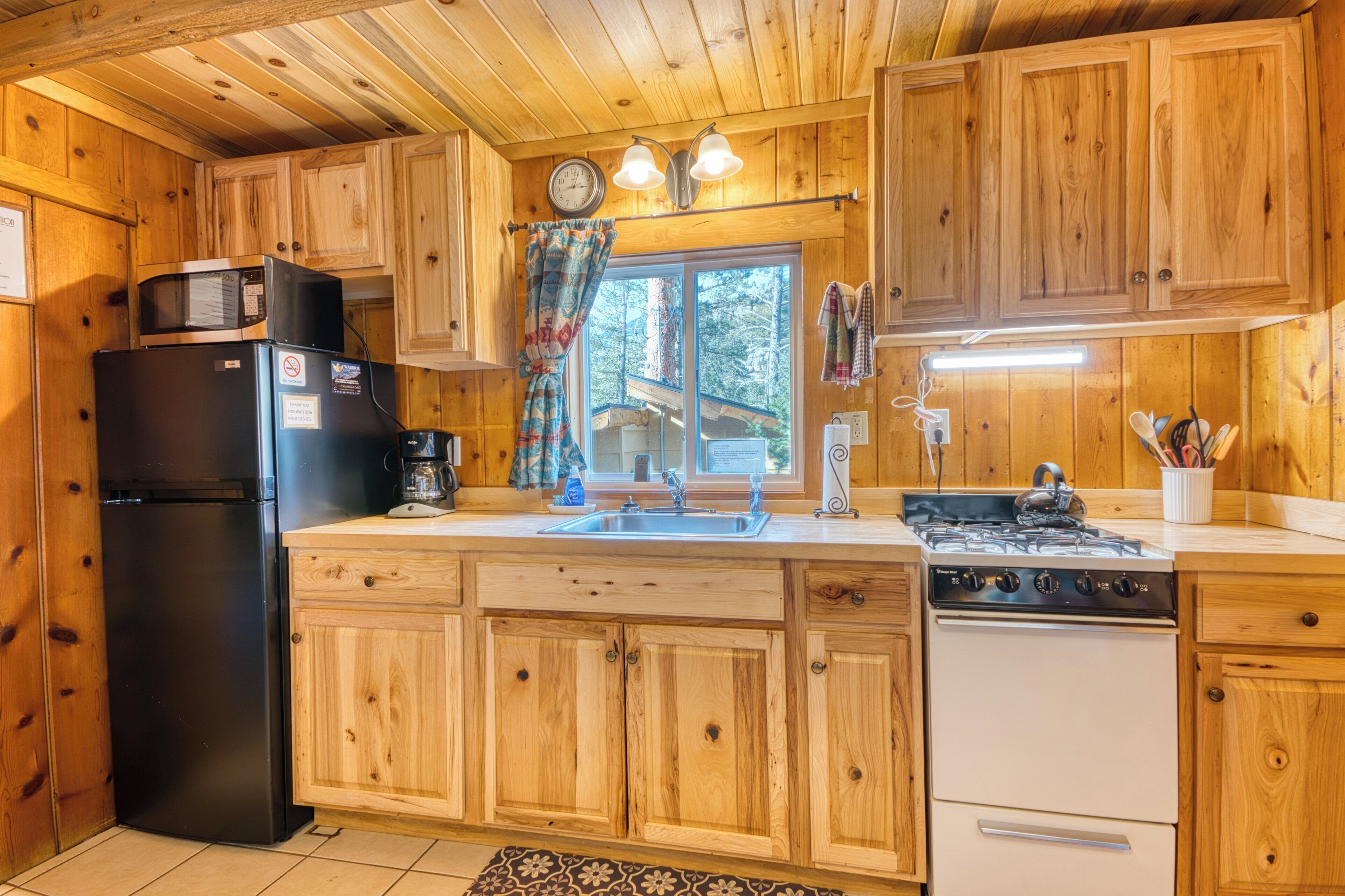 A wooden cabin kitchen with a refrigerator, stove, sink, and wooden cabinets.