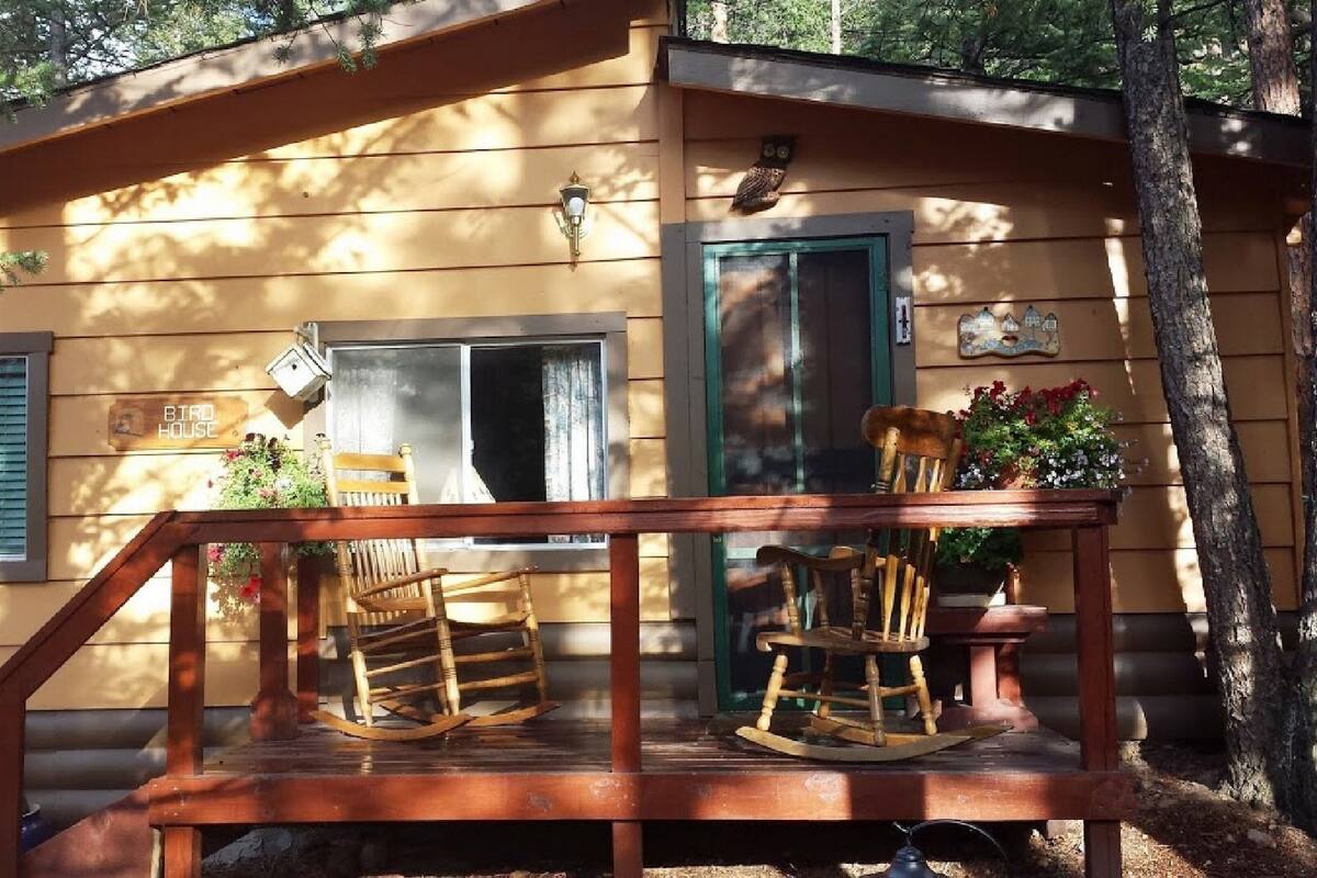 A rustic cabin with a porch, rocking chairs, and a birdhouse.