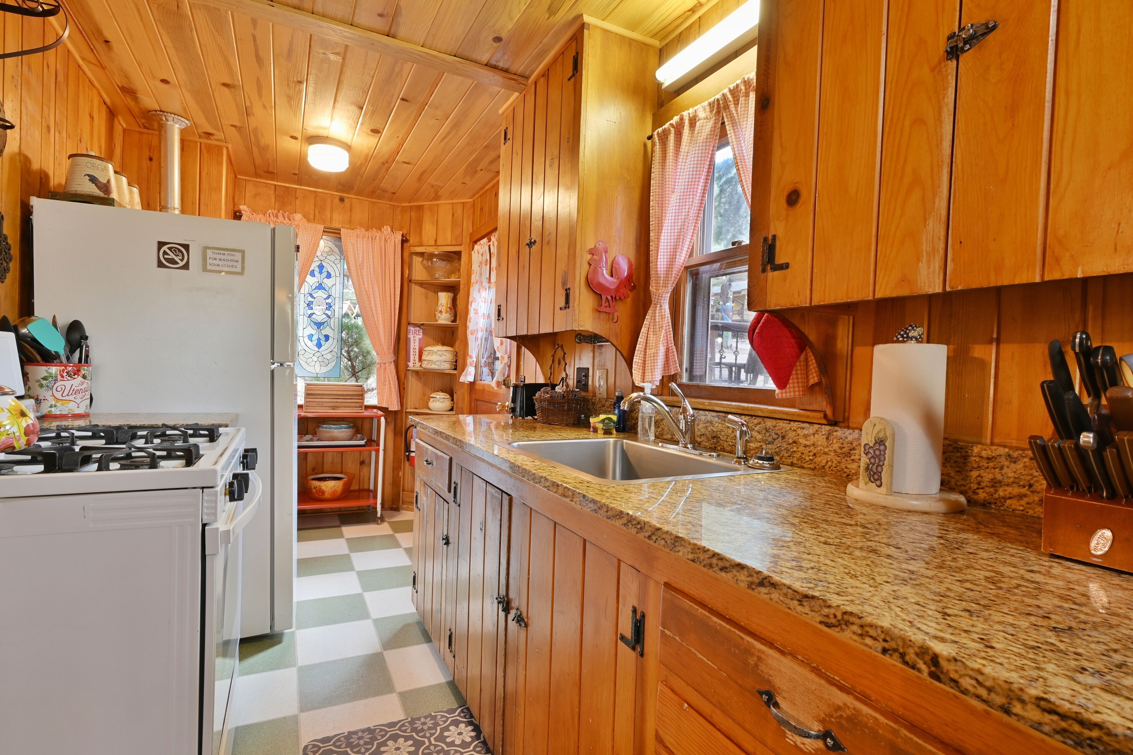 Une cuisine rustique, située dans une cabane en bois, équipée d’une cuisinière à gaz, d’un plan de travail en granit et de meubles de rangement en bois.