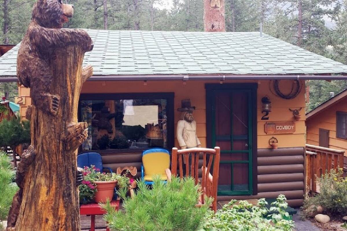 A rustic log cabin with a porch, a wooden chair, and a statue of a man.