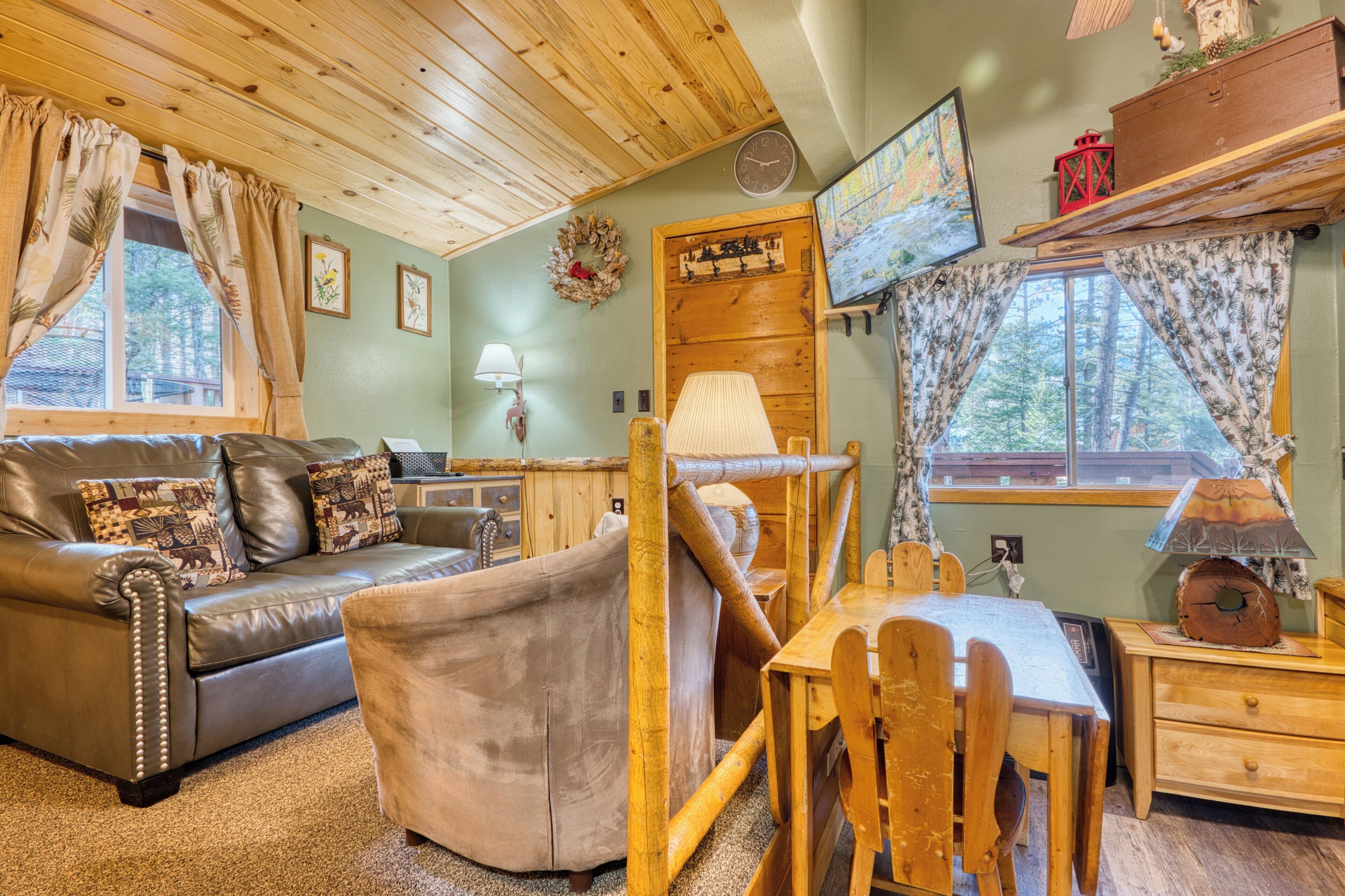 A cozy cabin interior with a leather sofa, a wooden dining table, and a TV mounted on the wall.