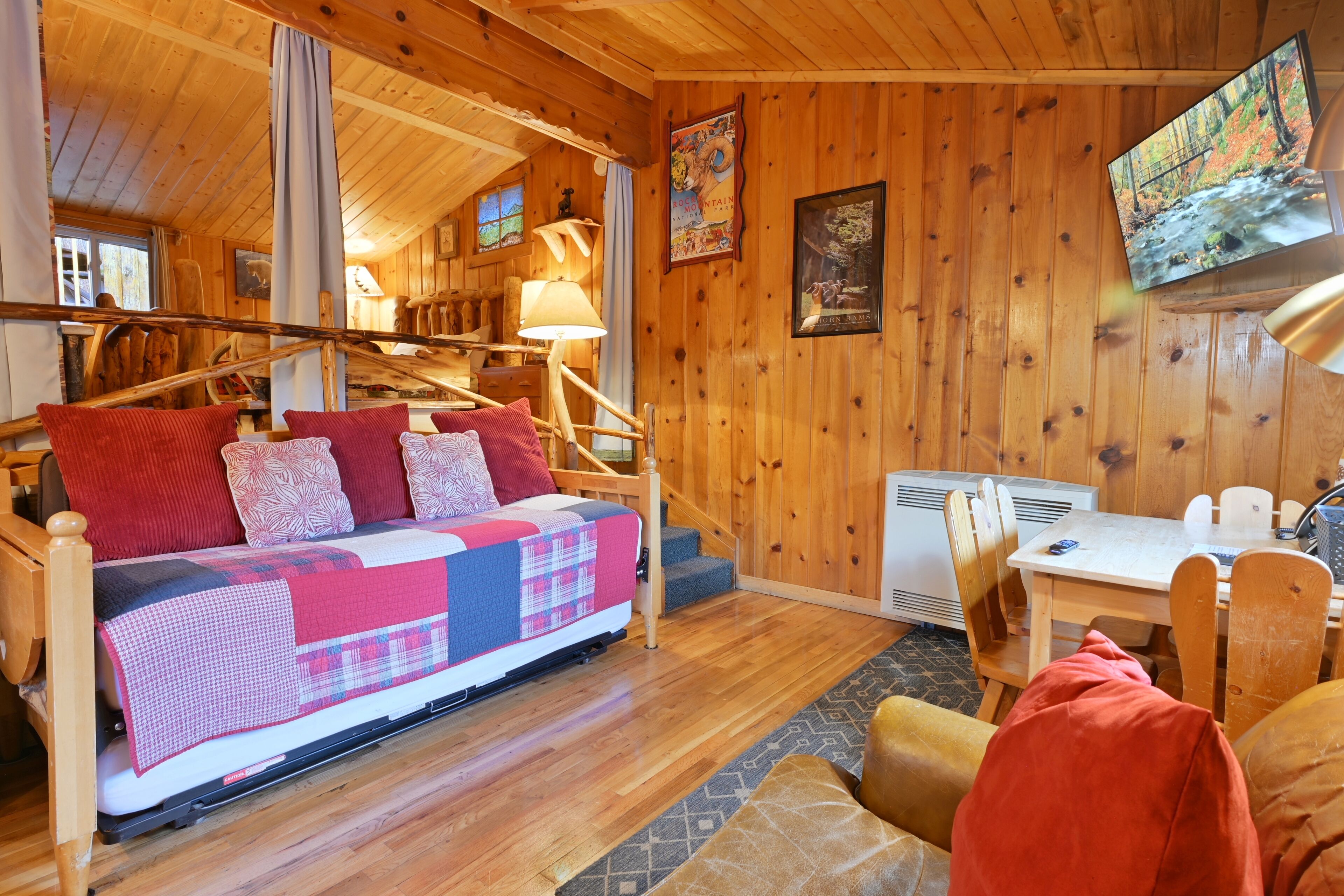 Une pièce chaleureuse, aménagée dans une cabane en bois, avec un lit, un bureau et un téléviseur fixé au mur.