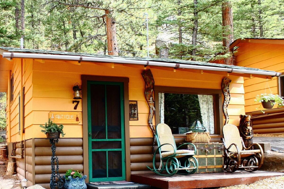 A rustic cabin with a green door, number 7, and a porch with two chairs and a table.