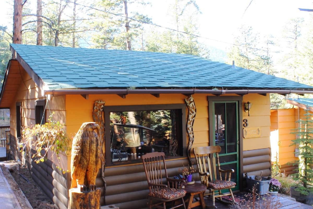A log cabin with a porch, wooden chairs, and a table.