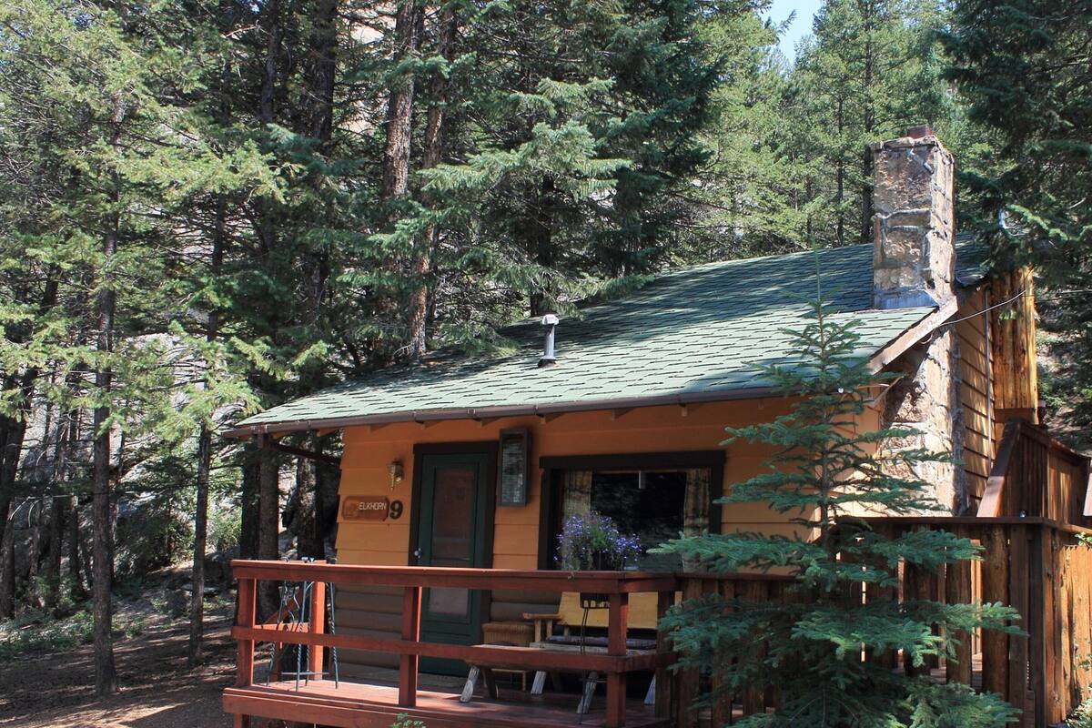 A cabin with a green roof, a porch with wooden railings, and a chimney.