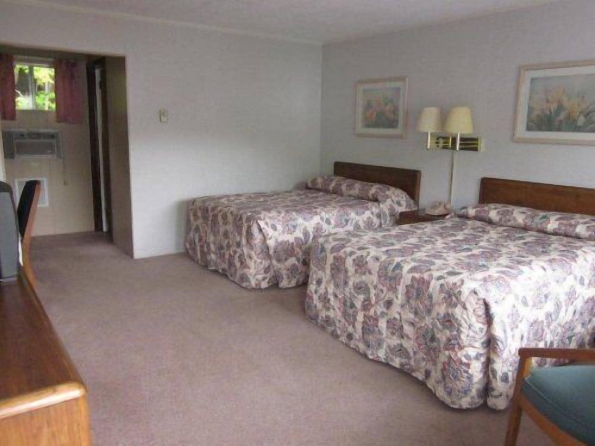 A bedroom with two beds, a desk, and a chair. There are two wall-mounted lamps and two framed pictures.