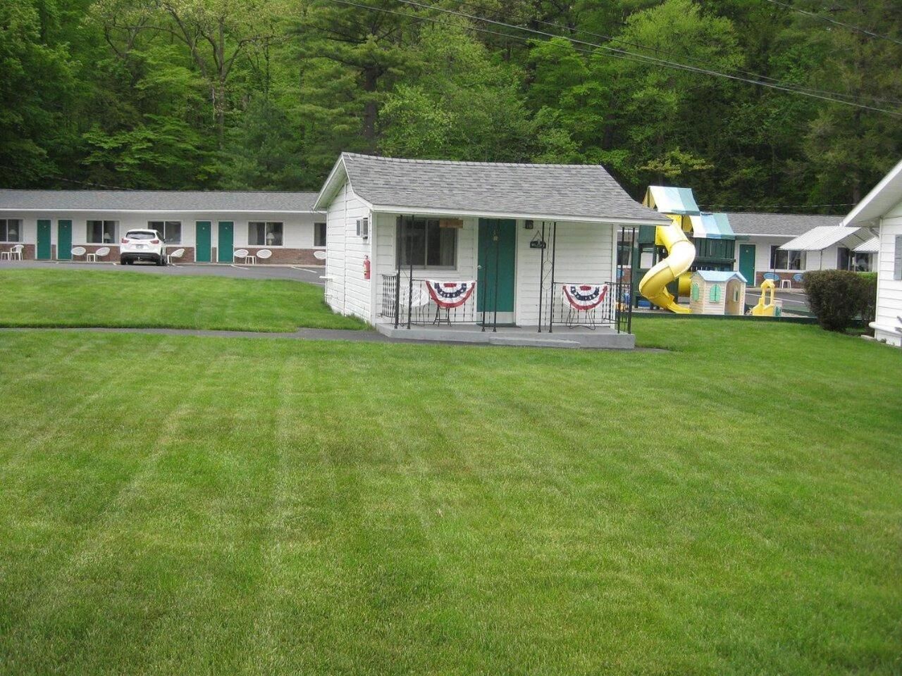 A motel with a small building, a covered parking area, and a playground.