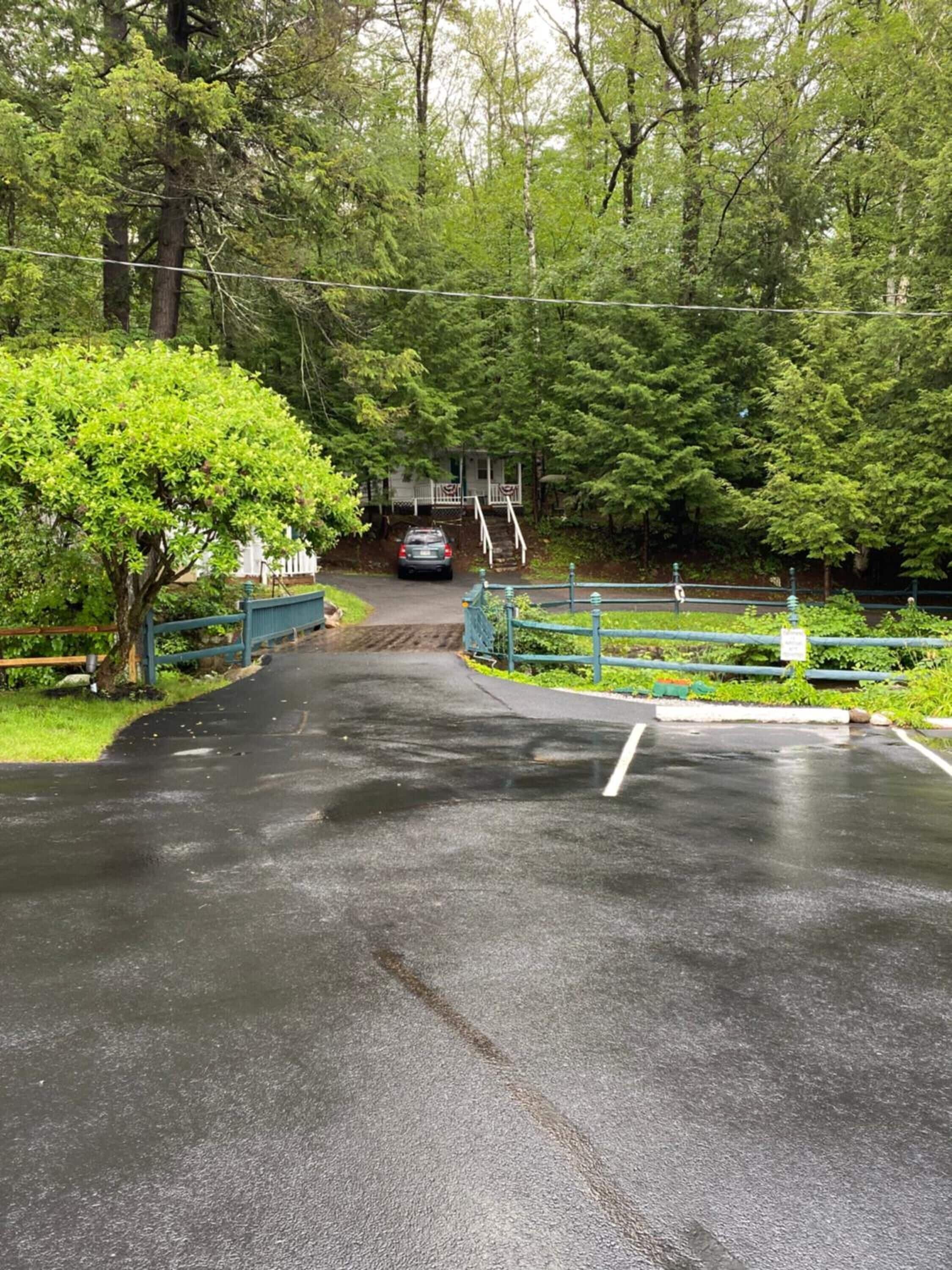A paved pathway leading to a building with a porch, surrounded by lush greenery.