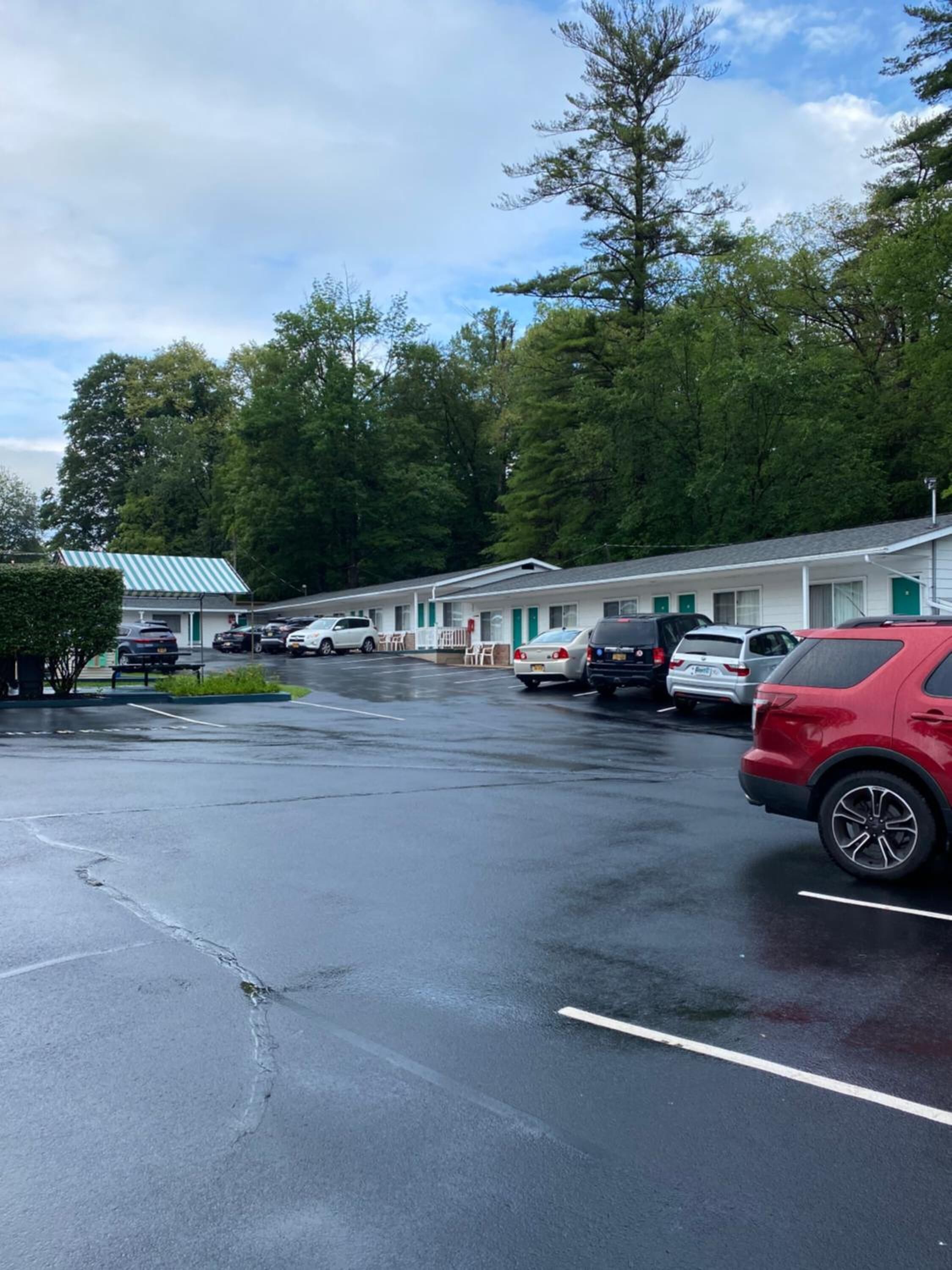 A motel with multiple rooms, a parking lot, and a green landscape.