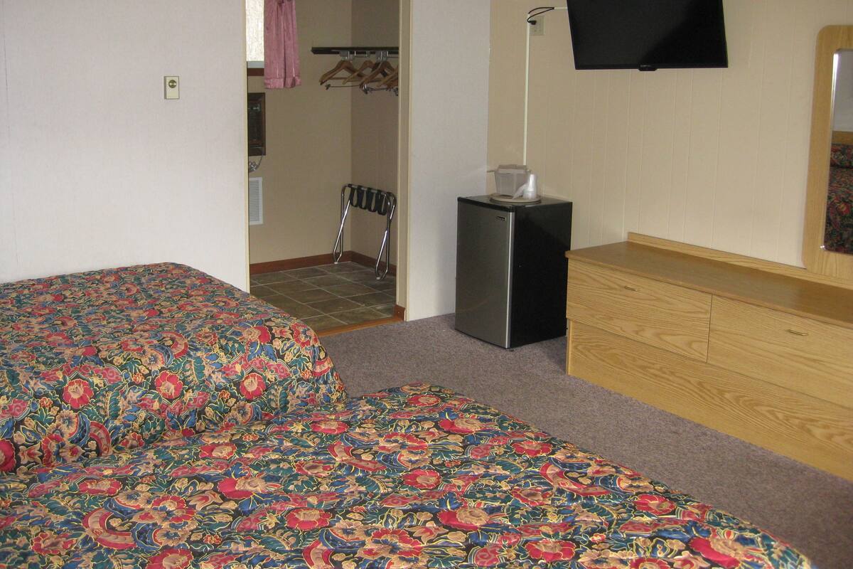 A room with two beds, a small refrigerator, a TV, and a wooden dresser.