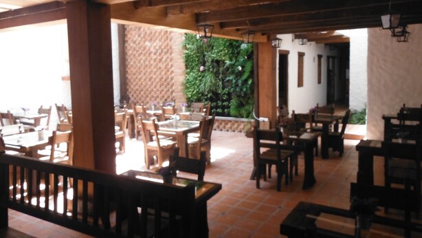 An indoor dining area with wooden tables and chairs, a brick wall, and a green plant wall.