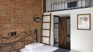 A room with a brick wall, a metal bed frame, a wooden ladder, and a framed picture on the wall.