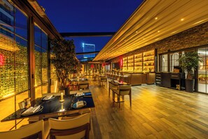Un restaurant moderne doté d’un bar, de planchers en bois et de grandes fenêtres offrant une vue sur le paysage urbain.