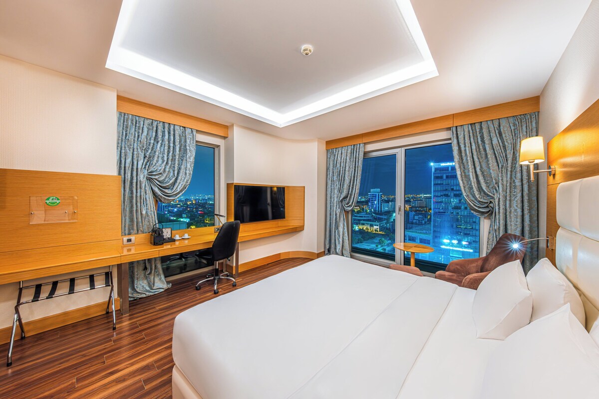 A hotel room with a bed, desk, chair, and a TV.