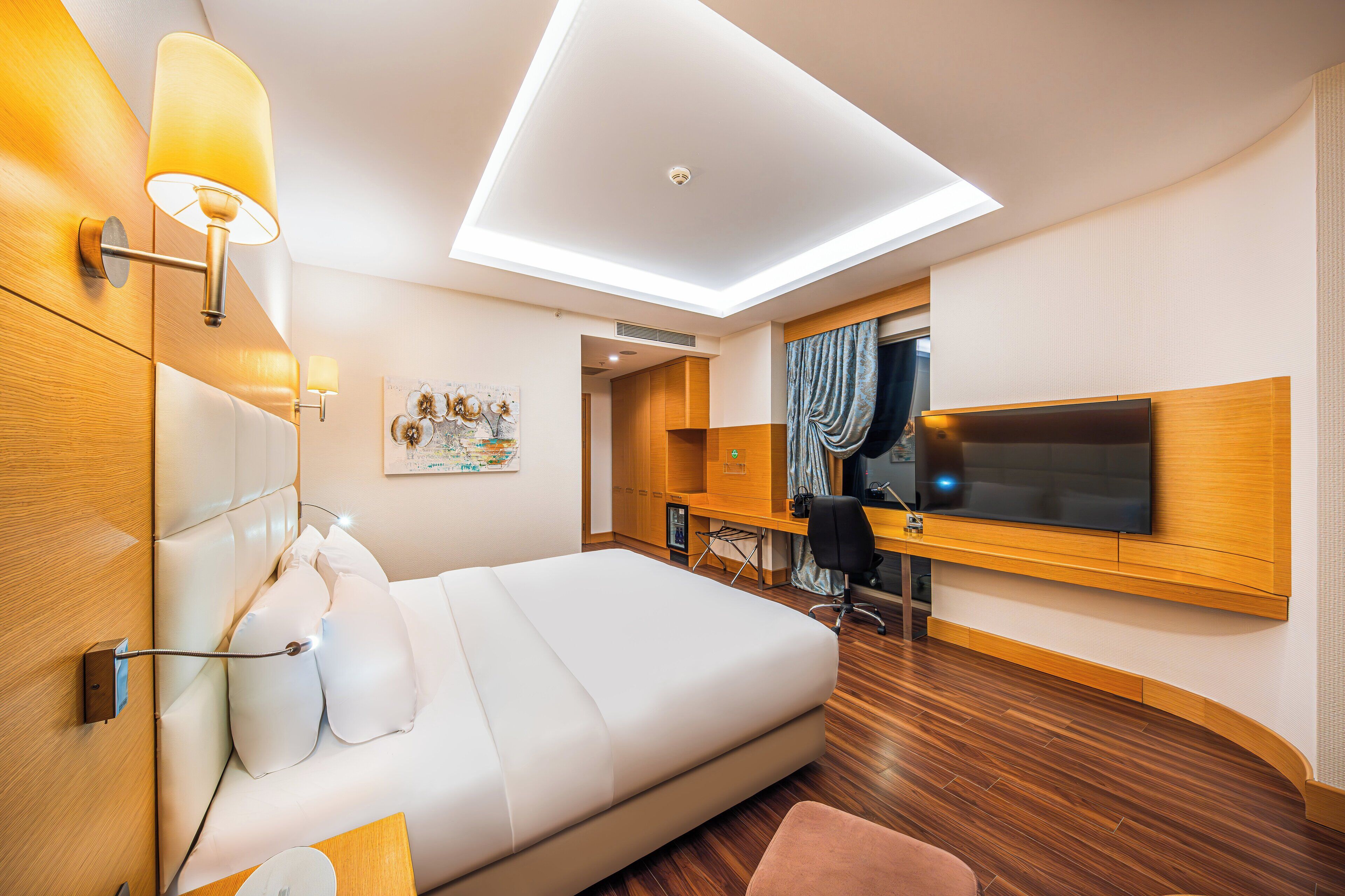 Una habitación de hotel moderna con una cama grande, un escritorio con televisor de pantalla plana y un tragaluz.