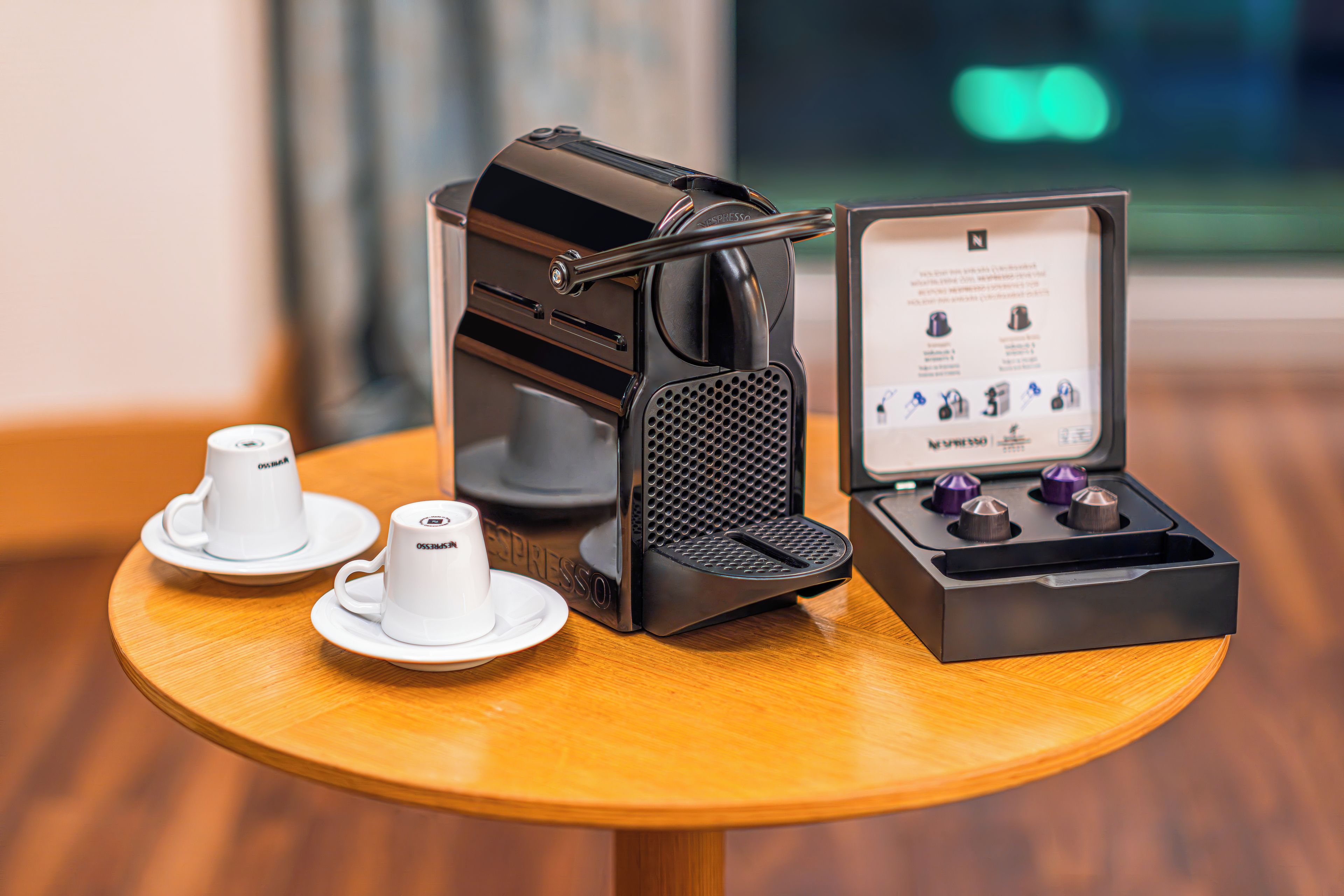 A coffee machine with a manual espresso maker, two white cups, and a box with instructions on a wooden table.