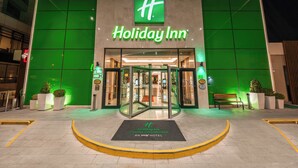 El exterior de un Holiday Inn con un llamativo logotipo verde, entrada de vidrio y fachada bien iluminada.