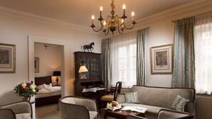 A well-appointed hotel room with a bed, a sitting area with a sofa and armchairs, a wooden desk, and a chandelier. - Palais Esplanade Hamburg - Adults Only (Hamburg)