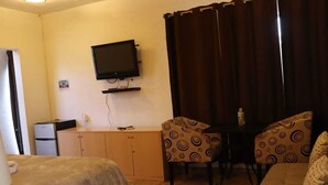 A room with a bed, a desk with two chairs, a television on the wall, a small refrigerator, and a curtain. - Finca Chipitlán Hotel (Cuernavaca)