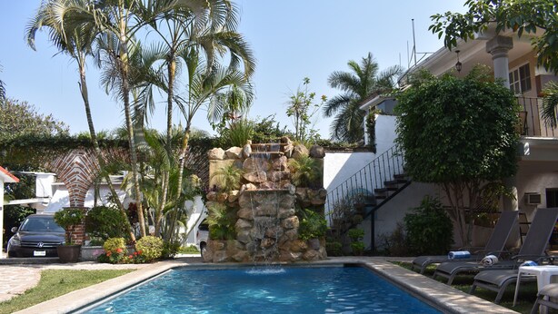 A swimming pool with a waterfall feature, surrounded by palm trees and a building with a staircase. - Finca Chipitlán Hotel (Cuernavaca)