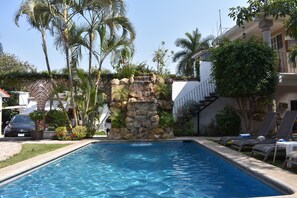 A swimming pool with a waterfall feature, surrounded by palm trees and a building with a staircase. - Finca Chipitlán Hotel (Cuernavaca)