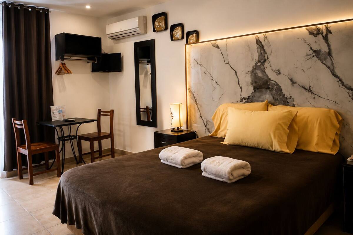 Una habitación de hotel con cama, escritorio, silla, televisor y aire acondicionado.