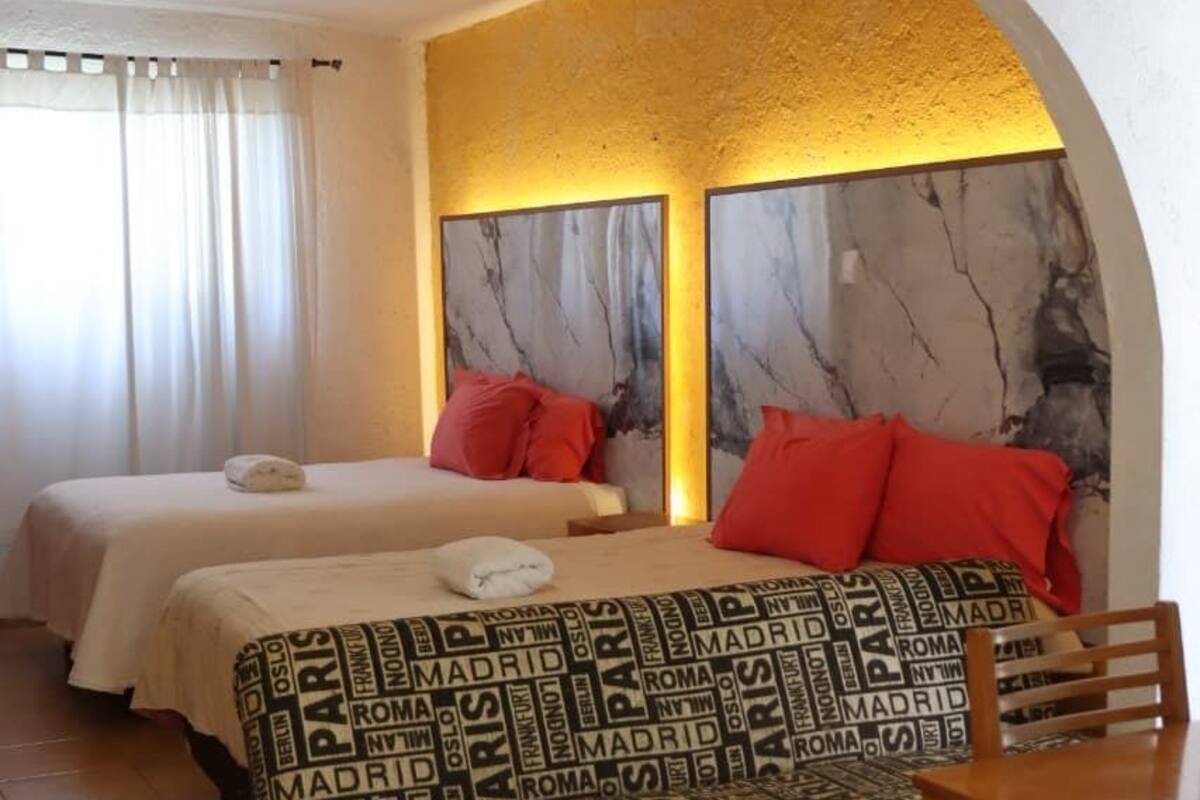 Habitación de hotel con dos camas, una mesa de comedor y un arco decorativo.