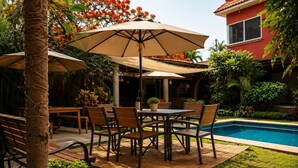 A patio with a pool, outdoor furniture, and a red building in the background. - Finca Chipitlán Hotel (Cuernavaca)