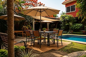 Um pátio com piscina, mobiliário de exterior e um edifício vermelho ao fundo.