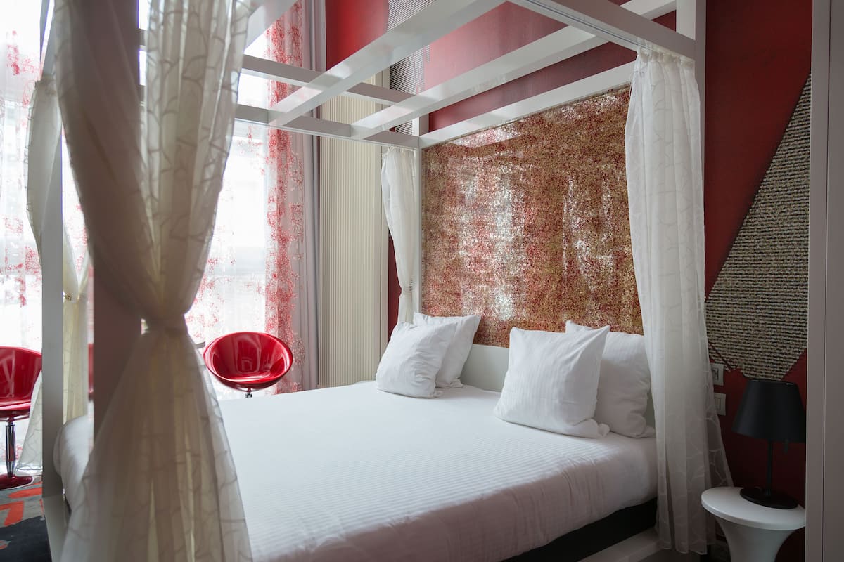 A bedroom with a canopy bed, white bedding, and a red textured wall.