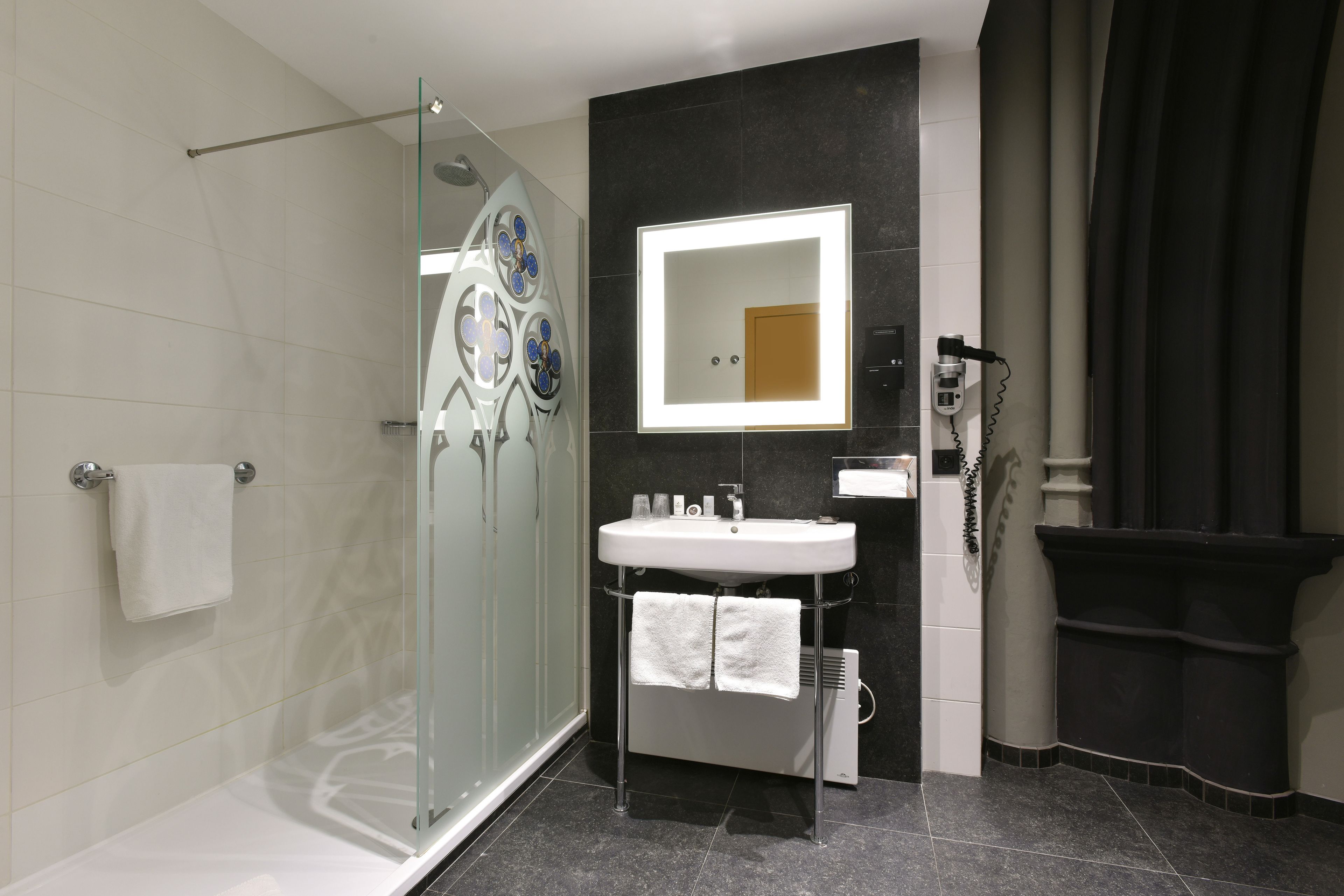 Un baño moderno con cabina de ducha de vidrio, un lavabo blanco con espejo y una pared revestida con baldosas oscuras.