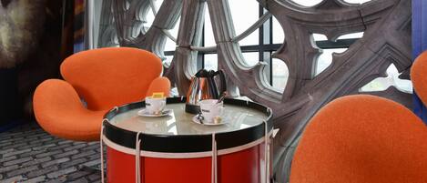 Una habitación con un ventanal grande y decorativo, un tambor rojo y sillas naranjas.