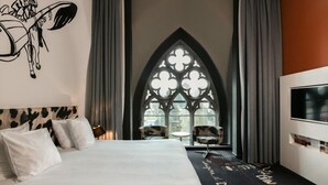 Une chambre avec un grand lit, une fenêtre de style gothique et un téléviseur fixé au mur.