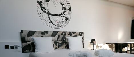 Habitación de hotel con cabecera estampada de vaca, ropa de cama blanca, una toalla y una obra de arte en la pared.
