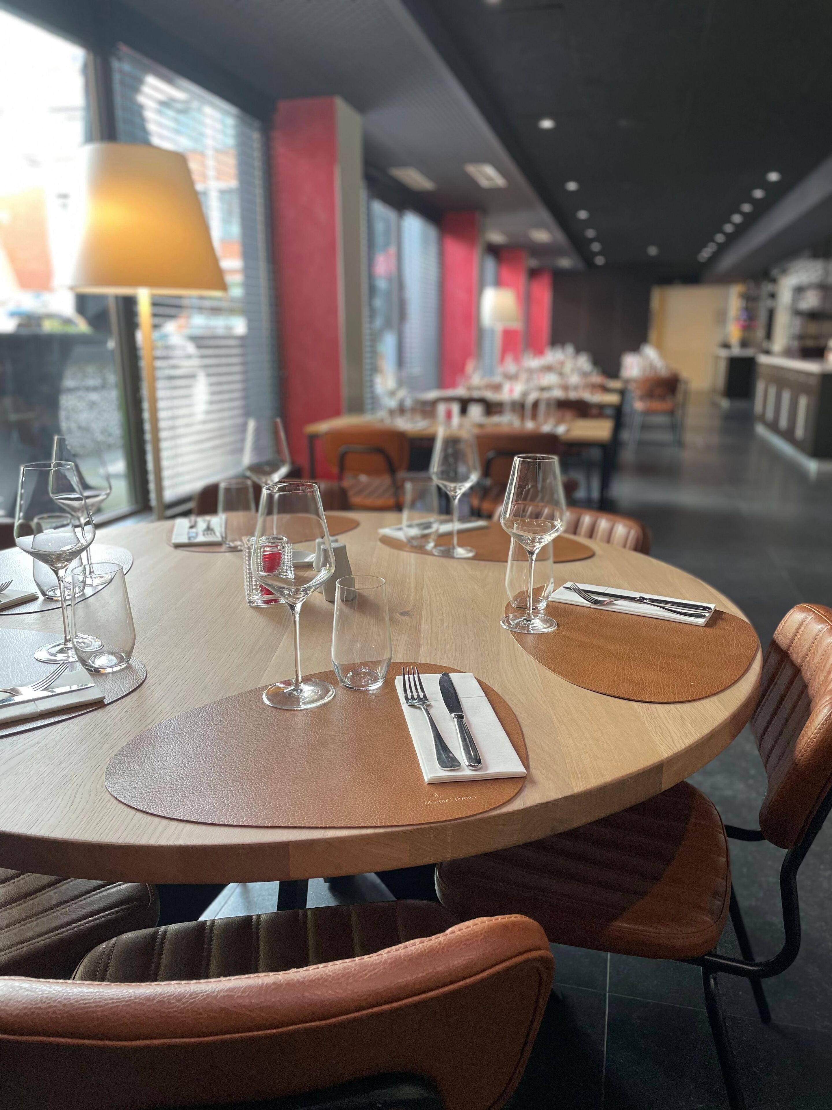 Een restaurant met ronde tafels, elk voorzien van wijnglazen, bestek en servetten.