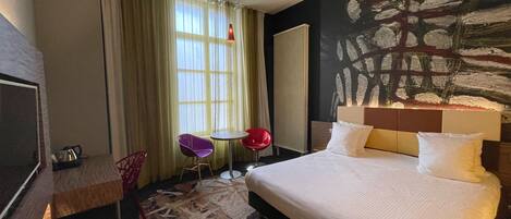 Habitación de hotel con una cama grande, un escritorio, una silla, una mesita y un cuadro en la pared.