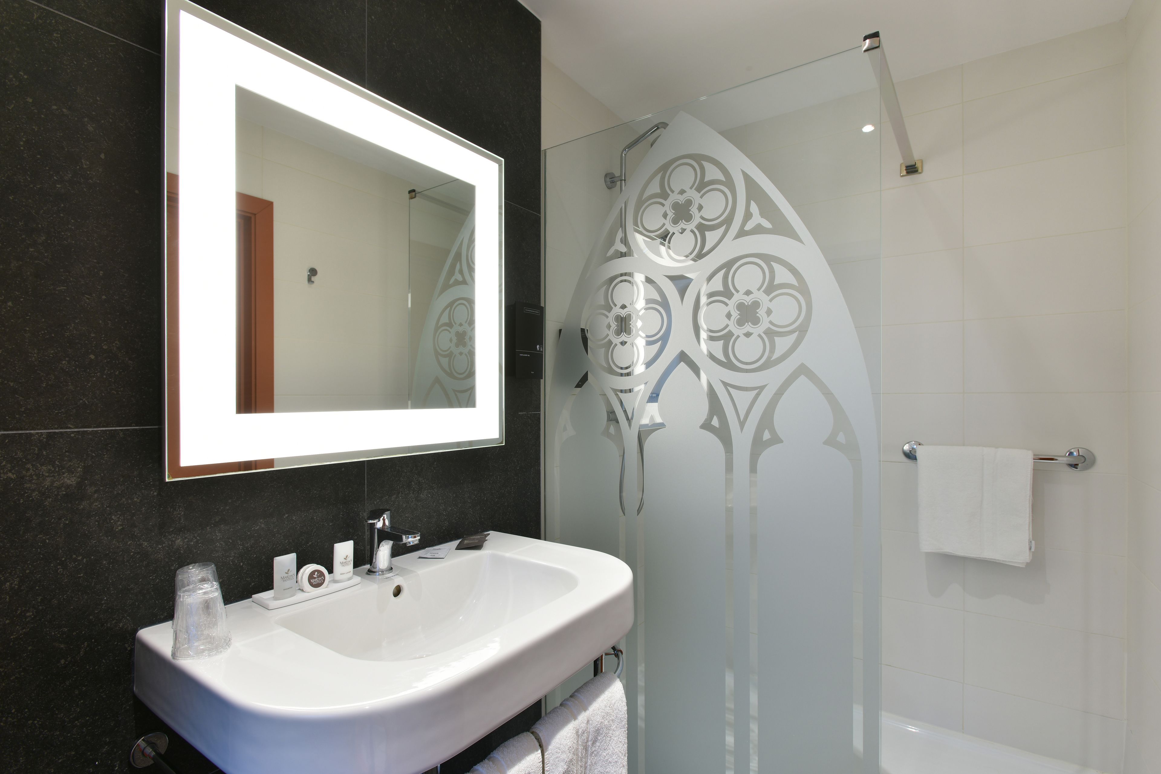 A modern bathroom with a large mirror, a white sink, and a glass shower enclosure.