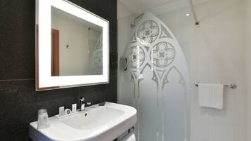 A modern bathroom with a large mirror, a white sink, and a glass shower enclosure.