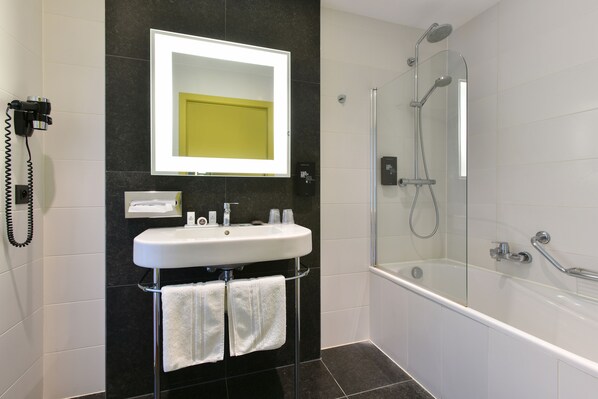 Un baño moderno con un lavabo blanco, un espejo grande, una ducha con cerramiento de vidrio y un teléfono en la pared.