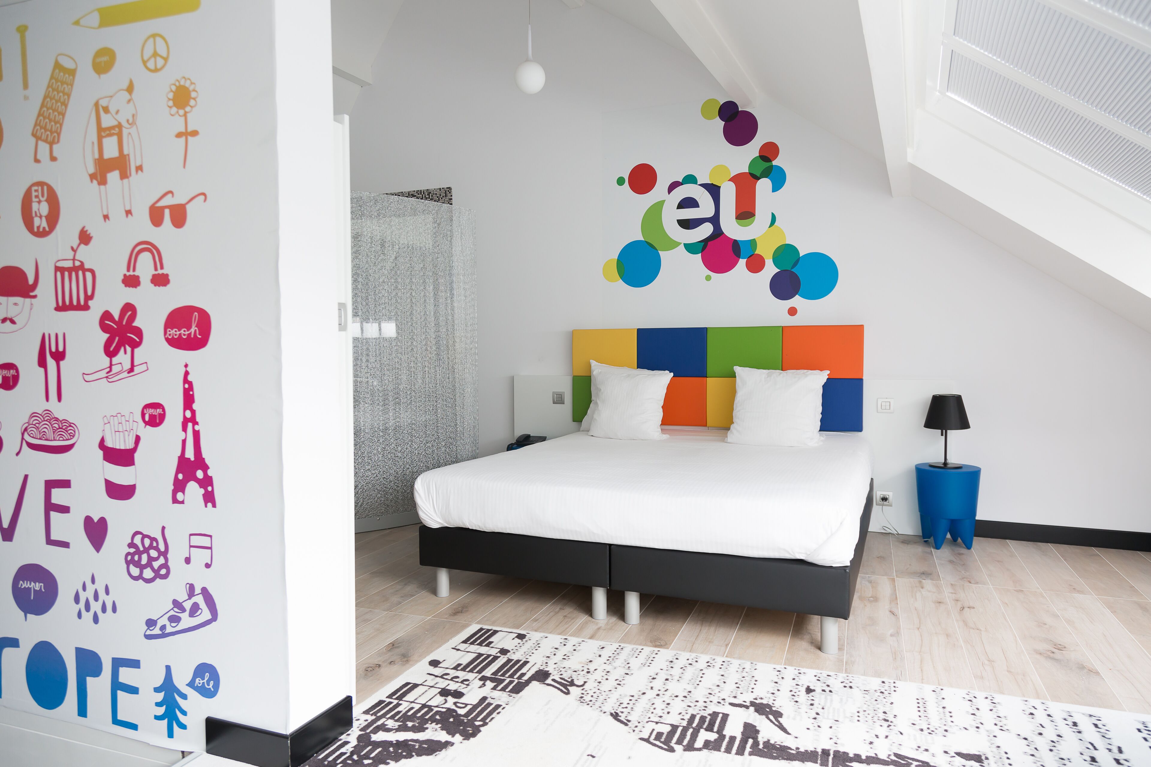 Un dormitorio moderno con una cama, una obra de arte colorida en la pared y una alfombra estampada.