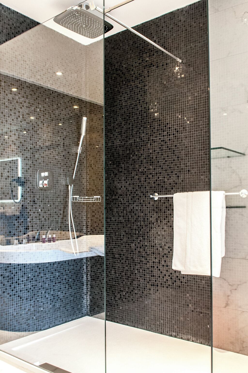 A modern bathroom with a glass shower enclosure, a bathtub, and a large mirror.