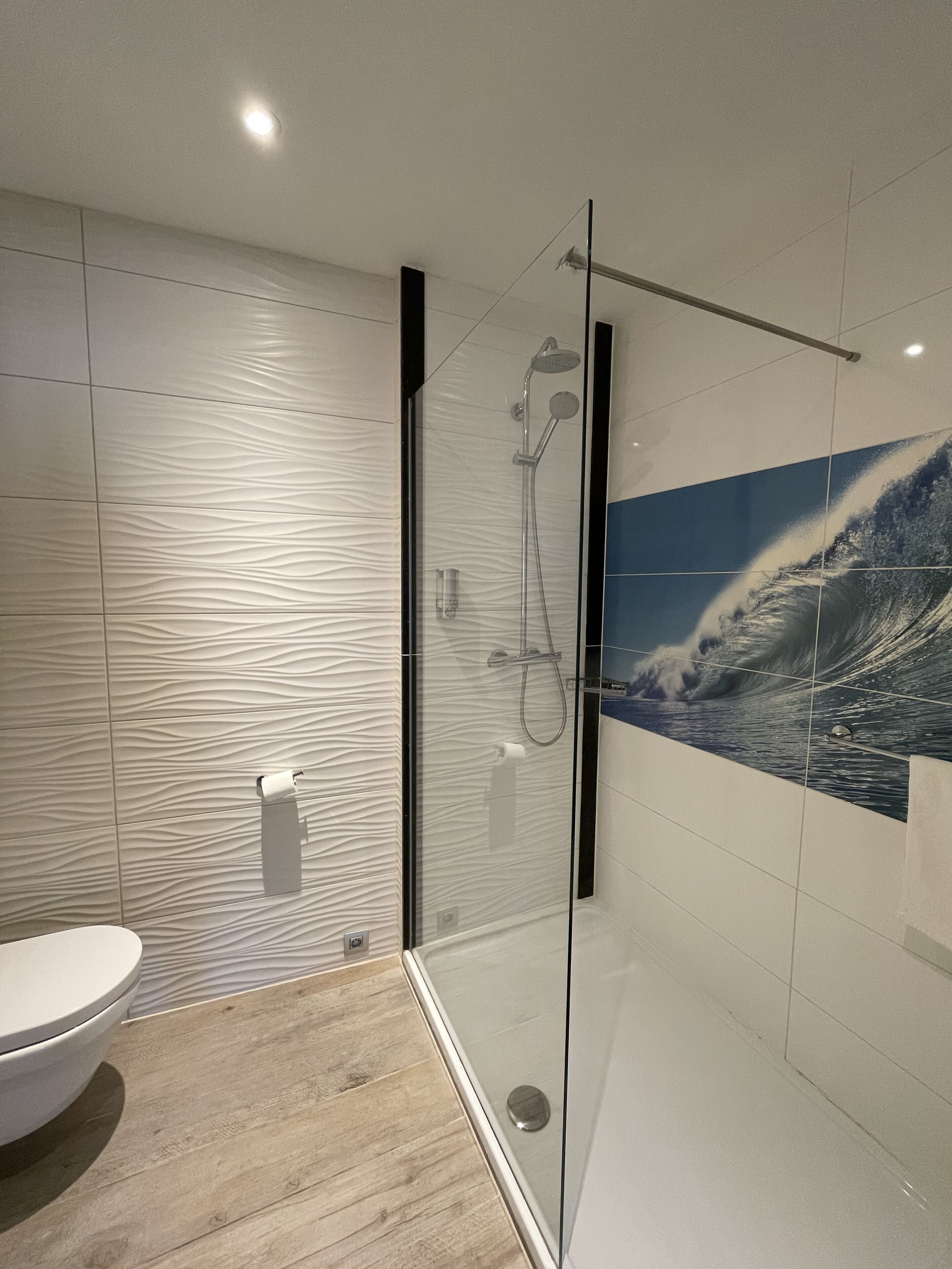 A modern bathroom with a glass-enclosed shower, a toilet, and a wall-mounted towel dispenser.
