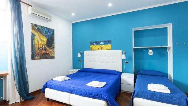 Une chambre d’hôtel avec un grand lit, un lit plus petit et une fenêtre avec des rideaux bleus.